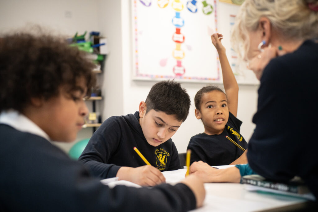 Photo of three children working with a tutor, one with her arm in the air